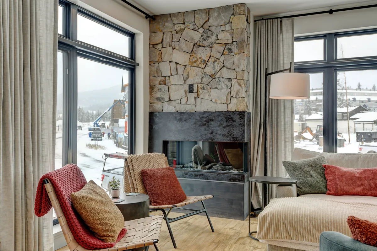 A cozy living area with a stone fireplace, large windows, and comfortable seating. The space is perfect for unwinding after a productive day, offering views to the outside and a relaxing atmosphere for reading or gathering with friends.