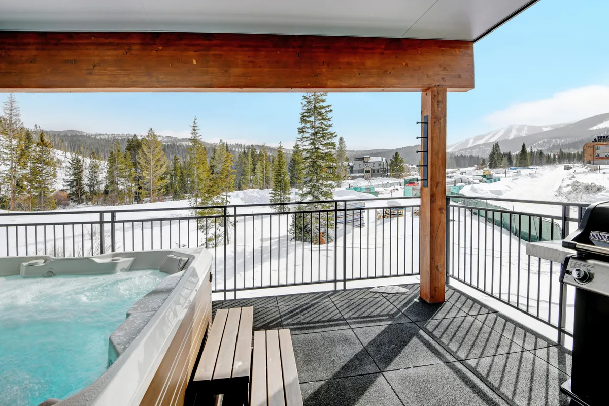 A hot tub nestled on a balcony with a sturdy wooden railing overlooks a peaceful, snow-covered landscape and distant tree line. The inviting water and outdoor barbecue hint at both relaxation and entertaining possibilities on the private balcony.