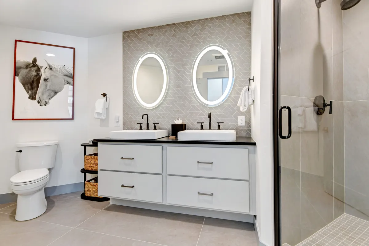A modern bathroom with elegant double sinks, oval mirrors, and striking horse artwork. The space feels serene and inviting, ideal for refreshing morning rituals or soothing evening routines.
