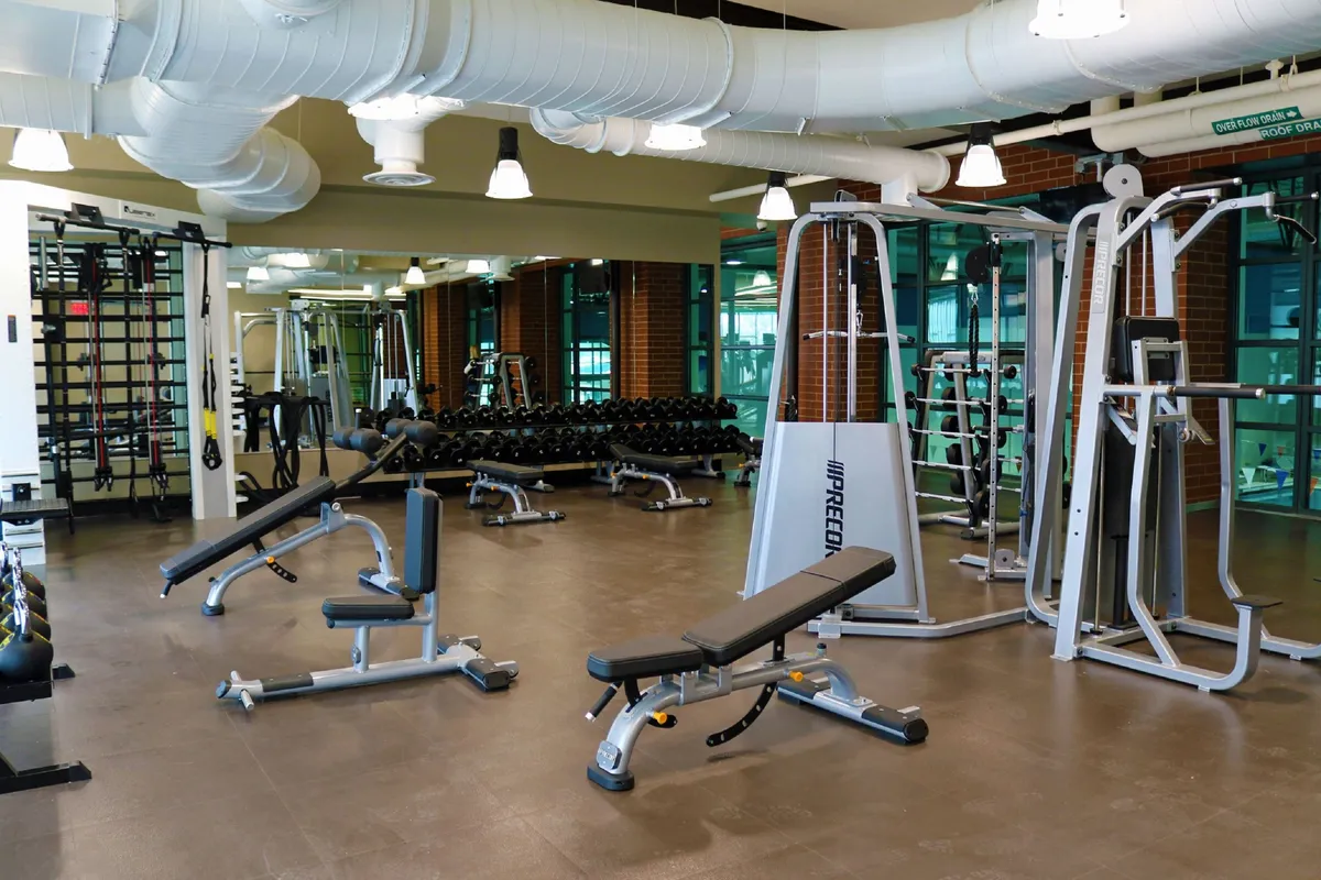 This interior shot displays a fitness area equipped with weightlifting equipment, exercise benches, and mirrored walls. The space is bright and motivating, suggesting a dedicated environment for maintaining wellness routines.