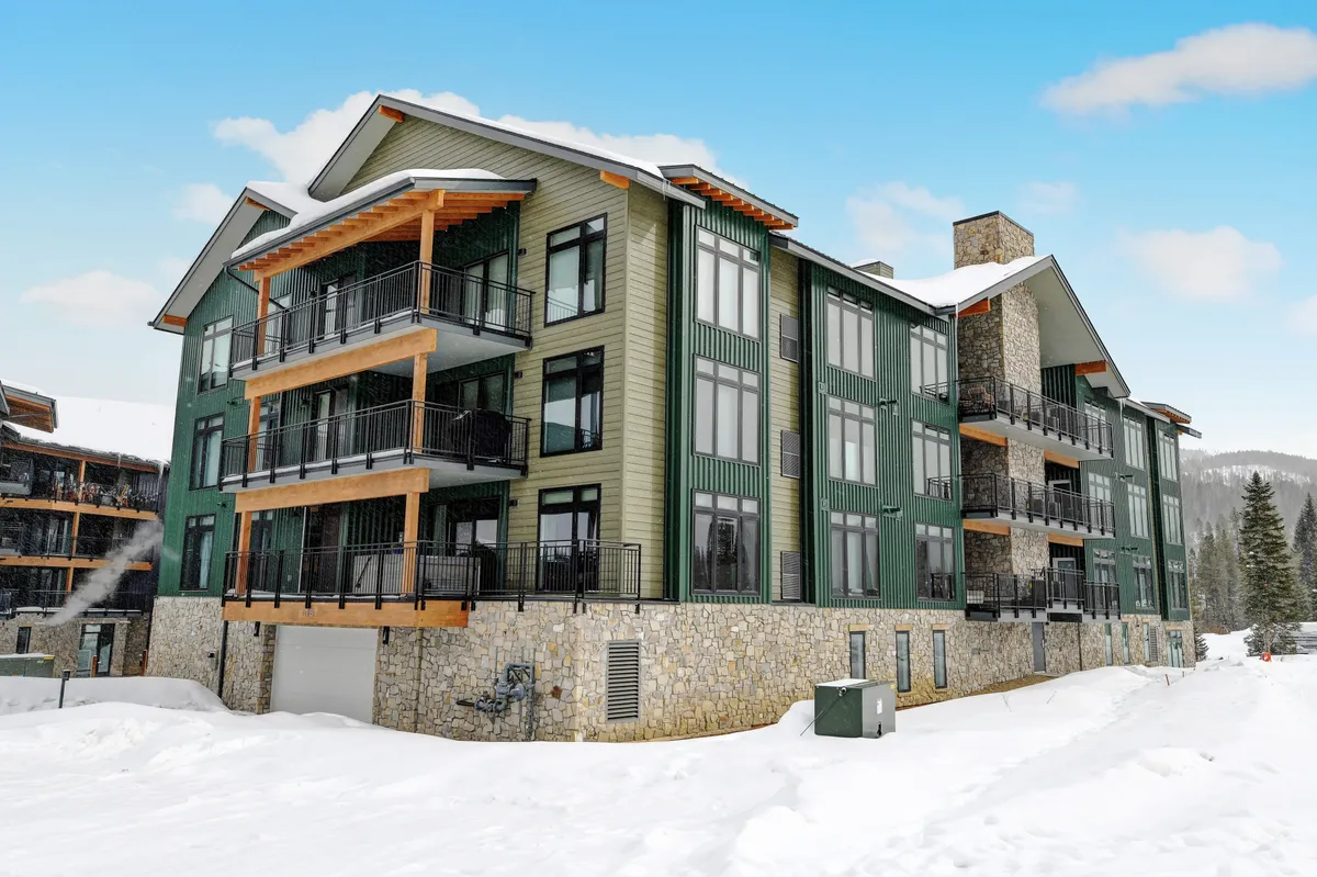This exterior image showcases the modern architecture of the condo, featuring large windows, stone accents, and wooden balconies. The surrounding snow and inviting appearance set the scene for mountain adventures and winter fun, reflecting the broader appeal for families and groups seeking year-round excitement.