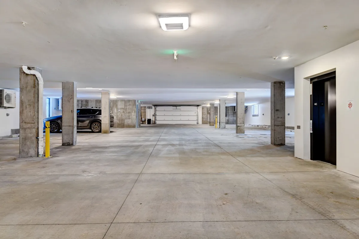 A modern, well-maintained heated garage with clearly marked parking spaces, support columns, and an elevator. The atmosphere is secure and accessible, designed for easy parking and transition in any season.