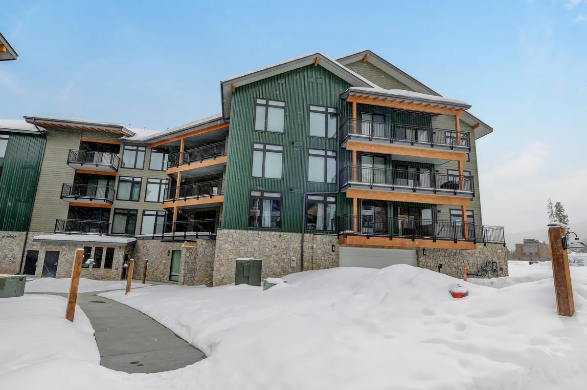 This exterior shot features the green and wood-accented building, balconies with railings, and a snowy landscape. The inviting mood suggests warmth and togetherness within, hinting at cozy evenings with hot cocoa after snowy adventures.