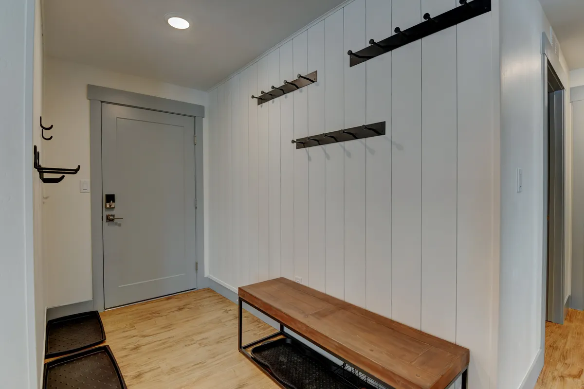Shows the organized entryway with a front door, coat hooks, and a wooden bench—an inviting spot for guests to gear up or return from outdoor adventures. The setup hints at routines involving storing ski or biking equipment and prepping for the day outside.